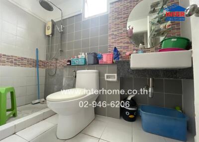 Modern bathroom with tiled walls, toilet, sink, mirror, and shower.