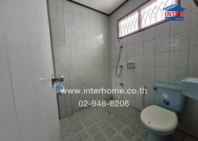 Bathroom with tiled walls and floor, shower area, toilet, and small window