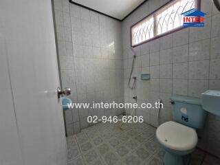 Bathroom with tiled walls and floor, shower area, toilet, and small window