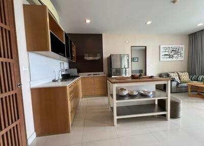 Modern kitchen area of a home with wooden cabinets, a center island, and adjacent living space