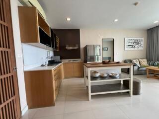 Modern kitchen area of a home with wooden cabinets, a center island, and adjacent living space