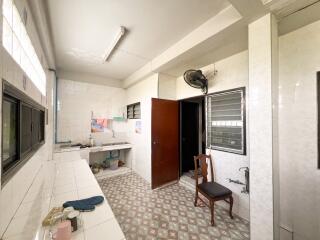 Spacious kitchen with tiled walls and floors, featuring multiple windows, a sink area, and a chair.