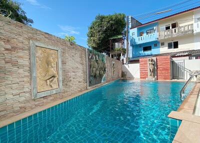 A private swimming pool with decorative wall art and surrounding buildings.
