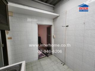 A utility room with tiled walls and flooring, featuring a sink and an open doorway to another room.