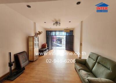 Spacious living room with wooden flooring, a light green sofa, various pieces of furniture, and large windows providing natural light