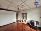 Living room with wooden flooring, white walls, ceiling tiles, a chair, and a small shelving unit.