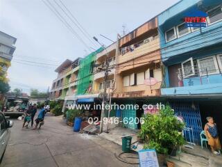 Street view of colorful residential buildings with people and plants.