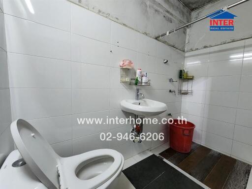 A bathroom with a toilet, sink, and red bucket