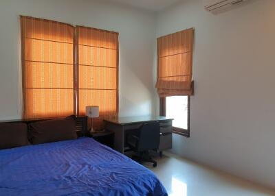 Bedroom with blue bedspread, desk, chair, and windows with orange curtains