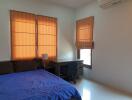 Bedroom with blue bedspread, desk, chair, and windows with orange curtains