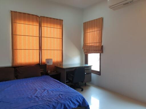 Bedroom with blue bedspread, desk, chair, and windows with orange curtains