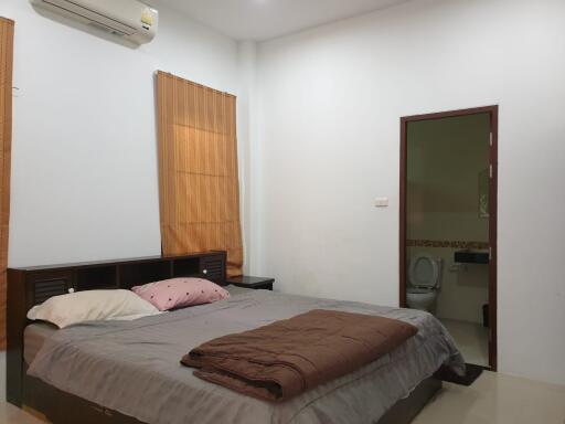 A bedroom with a bed, pillows, brown blanket, air conditioner, and en-suite bathroom.