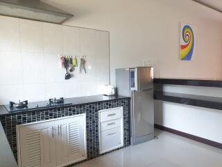 Modern kitchen with dual burner stove, overhead hood, refrigerator, and colorful wall art