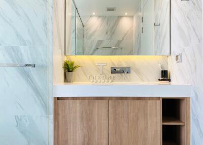 Modern bathroom with a large mirror, wooden cabinet, and marble walls