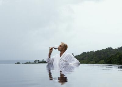 Person relaxing in an infinity pool with a drink, overlooking scenic natural landscape