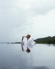 Person relaxing in an infinity pool with a drink, overlooking scenic natural landscape