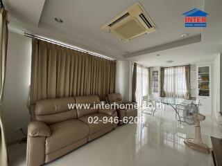 Living room with beige sofa, glass dining table, and large windows with beige curtains