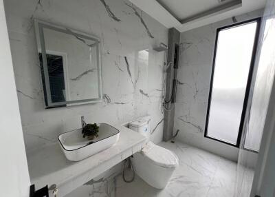 Modern bathroom with marble tiles, a large mirror, a sink, a toilet, and a window.