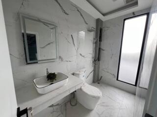 Modern bathroom with marble tiles, a large mirror, a sink, a toilet, and a window.