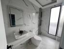 Modern bathroom with marble tiles, a large mirror, a sink, a toilet, and a window.