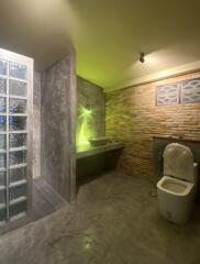 Modern bathroom with stone and brick accents, featuring a toilet, sink, and a glass block shower area