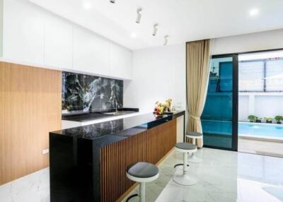 Modern kitchen with countertop and bar stools, adjacent to a pool area