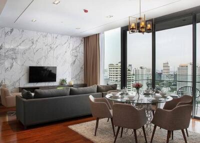 Spacious living room with a dining area, a large sectional sofa, wall-mounted TV, and floor-to-ceiling windows overlooking the city
