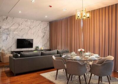 Modern living room with grey sofa, wall-mounted TV, round dining table, and elegant chandelier