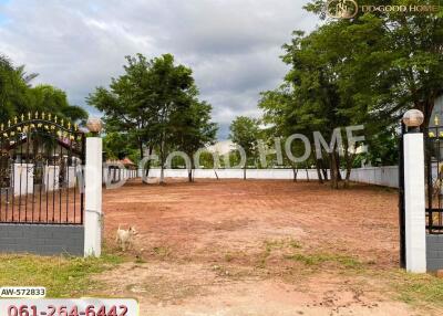 A vacant plot of land with surrounding trees and a gated entrance.