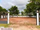 A vacant plot of land with surrounding trees and a gated entrance.