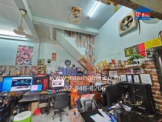 Cluttered workspace with multiple desks, computers, and wall decor