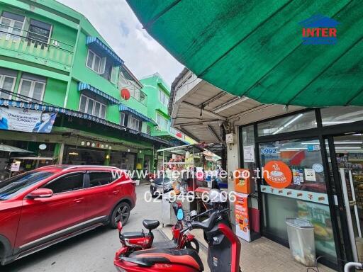 Street view with storefronts, cars, and motorcycles