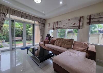 Spacious living room with large windows, L-shaped sofa, and glass doors leading to a garden.