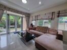 Spacious living room with large windows, L-shaped sofa, and glass doors leading to a garden.