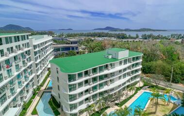 Overview of modern apartment buildings with green roofs, swimming pools, and a sea view in the background