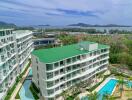 Overview of modern apartment buildings with green roofs, swimming pools, and a sea view in the background