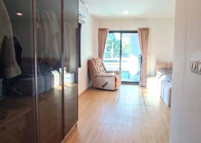 Spacious bedroom with wooden flooring, large wardrobe, recliner, and balcony access with curtain-covered glass doors