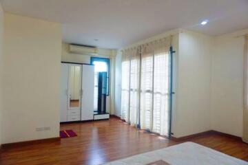 Spacious bedroom with wooden flooring, large windows with sheer curtains, and air conditioning.