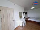 Bedroom with a wooden floor and white walls, featuring a bed, door, TV, mirror, and storage units.