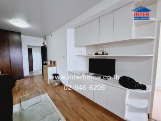 Modern living room with wooden flooring, built-in white cabinets, and a wall-mounted TV