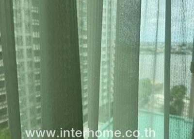 View from a window with sheer curtains overlooking other buildings and water