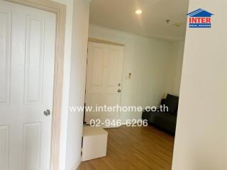 Living room with wooden flooring, white door, and minimal furniture