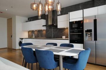 Modern kitchen and dining area with blue chairs, large fridge, and stylish lighting