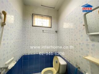 Bathroom with blue and white tiles, small window, toilet, and wall-mounted mirror