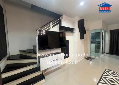 Modern living room with staircase, TV, and access to kitchen area