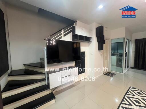 Modern living room with staircase, TV, and access to kitchen area