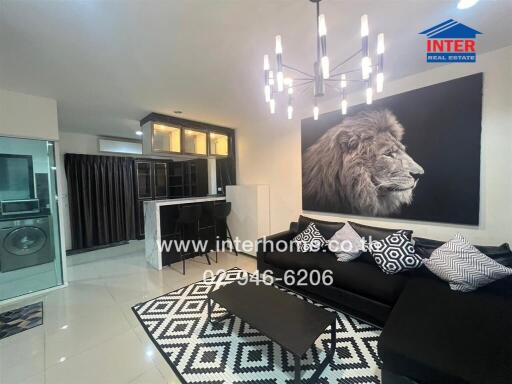 Modern living room with black sofa, patterned rug, wall art, and chandelier