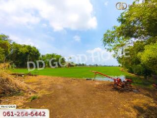 A vast green field with some farm equipment and trees under a clear sky.