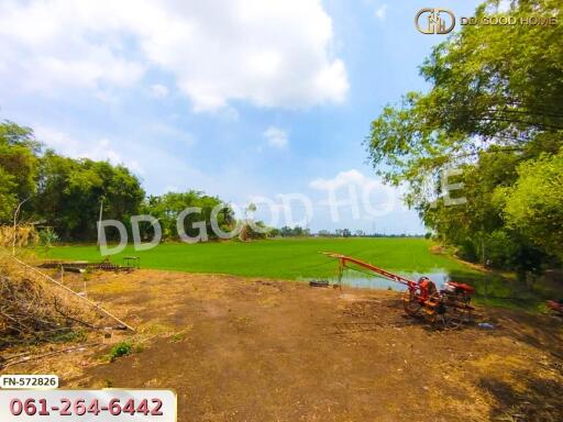 A vast green field with some farm equipment and trees under a clear sky.