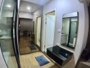 A modern hallway featuring a wall mirror, wooden flooring, and a doorway leading to another room